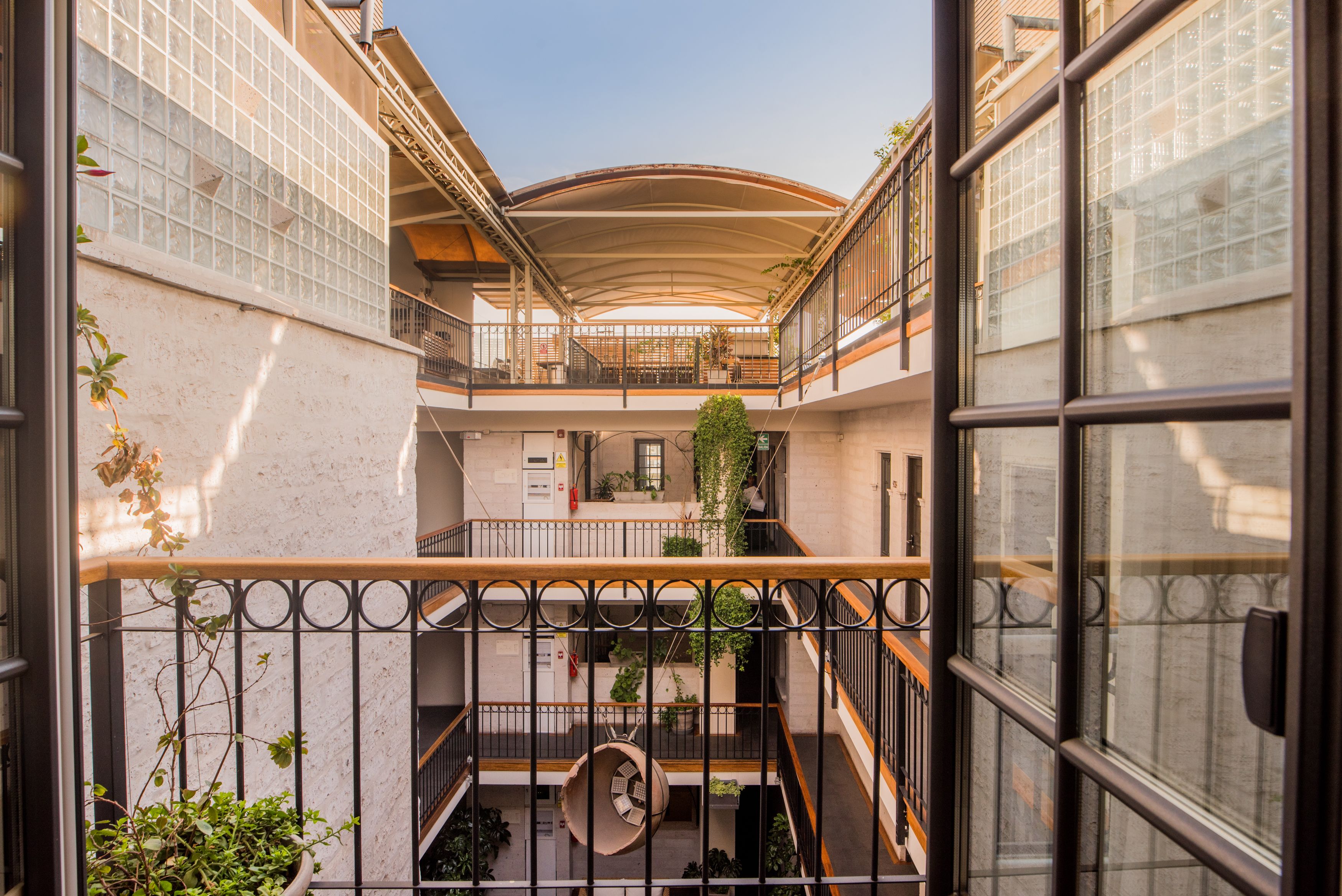 Ein mehrgeschossiges Atrium mit einer zentralen Wendeltreppe, Balkonen mit Metallgeländern und Topfpflanzen.