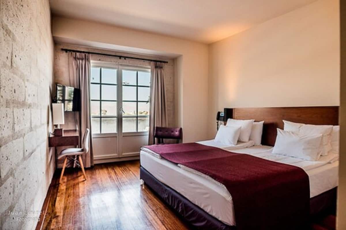 A hotel room with a large bed, a desk, a chair, and a window with curtains.