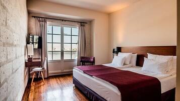 A hotel room with a large bed, a desk, a chair, and a window with curtains.