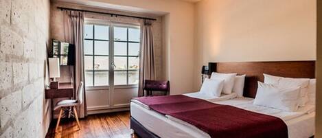A hotel room with a large bed, a desk, a chair, and a window with curtains.