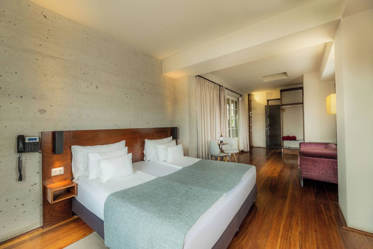 A hotel room with a large bed, a bedside telephone, a small table with a chair, and a purple armchair.
