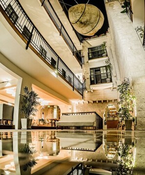 Un atrio de varios niveles con una piscina reflectante central, balcones y una mezcla de elementos arquitectónicos modernos y tradicionales.