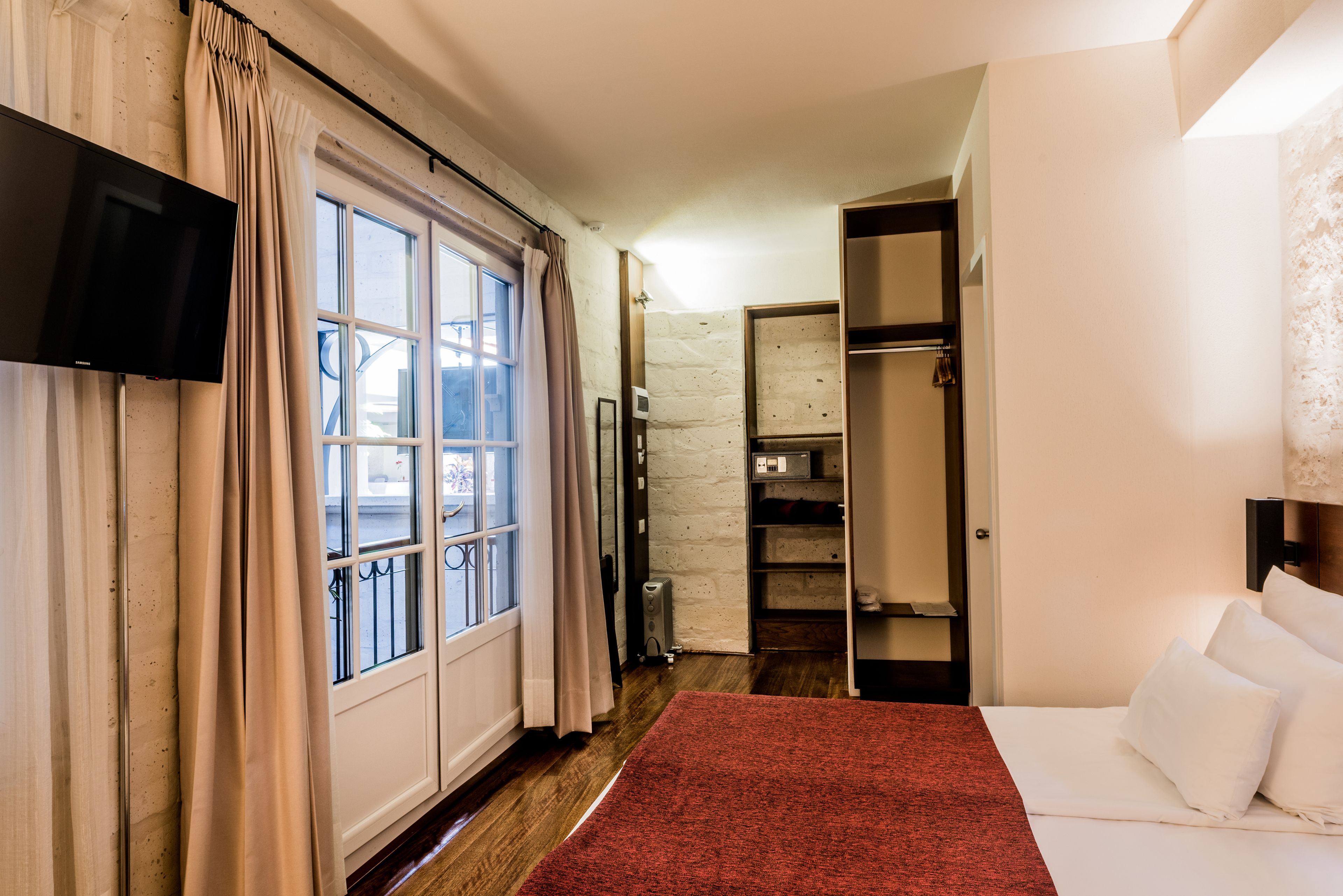 A hotel room with a bed, a TV, a wardrobe, and a window with curtains.