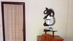 Ein Zimmer mit Holztisch und Stuhl, einem Spiegel mit Zierrahmen, einer kleinen Ablage mit Flaschen und einem Mülleimer.
