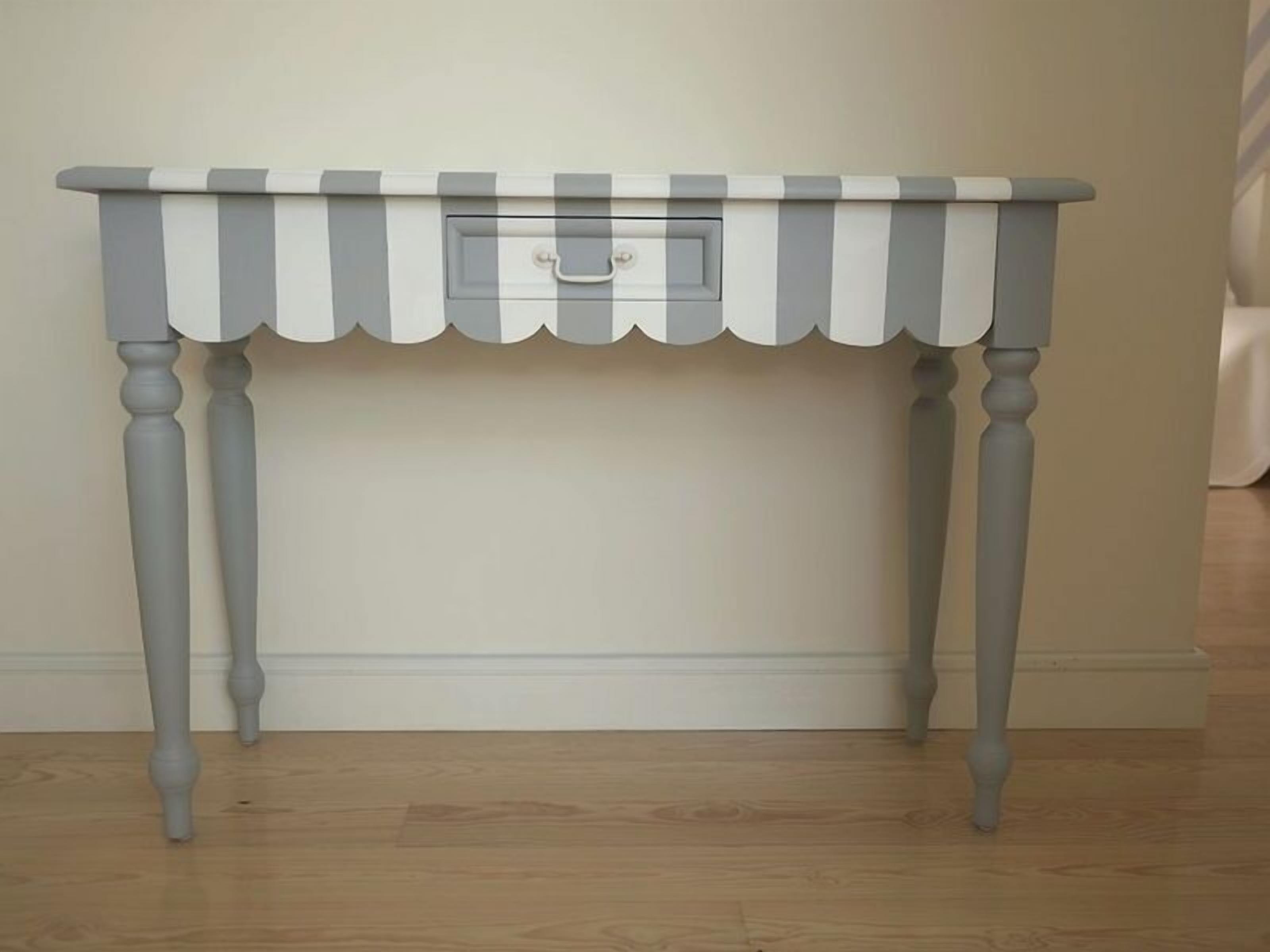A grey and white striped table with a single drawer against a plain wall.