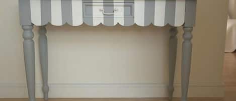 A grey and white striped table with a single drawer against a plain wall.