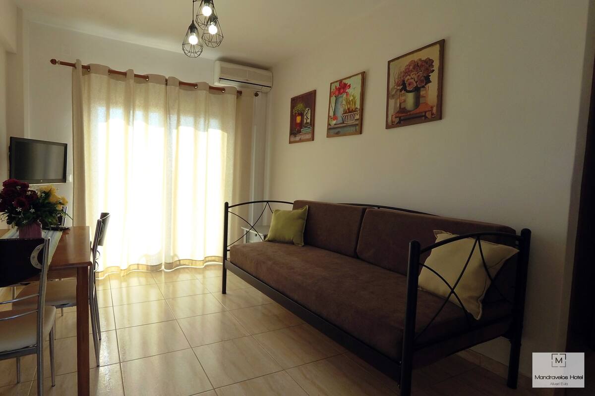 Una sala de estar con un sofá, una mesa de comedor con sillas, un televisor y una ventana con cortinas.