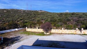 Blick auf ein Anwesen mit einer Steinmauer, einem Baum und einer hügeligen Landschaft im Hintergrund.