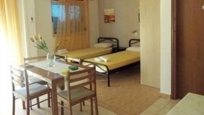 Ein kleines Zimmer mit zwei Einzelbetten, einem Holztisch mit Stühlen und einem Fenster mit Vorhängen.