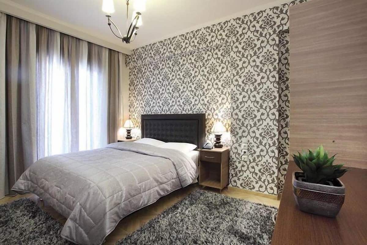 A bedroom with a bed, nightstands, a potted plant, and patterned wallpaper.