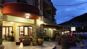 A hotel lobby with stone flooring, outdoor seating, and a large red circular light fixture. - Delfini Hotel (Amfilochia)