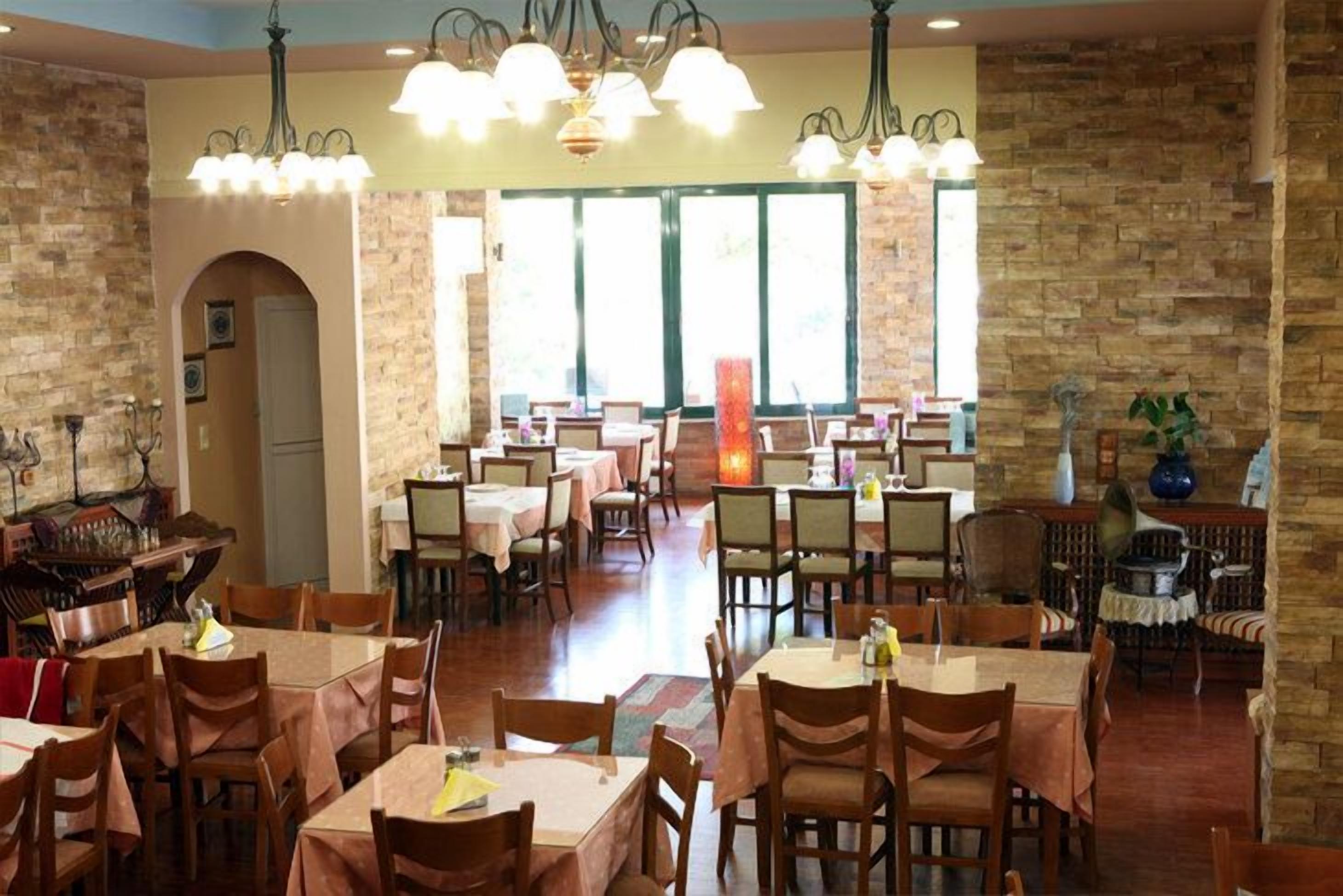 A restaurant with multiple tables and chairs, stone walls, and hanging light fixtures.