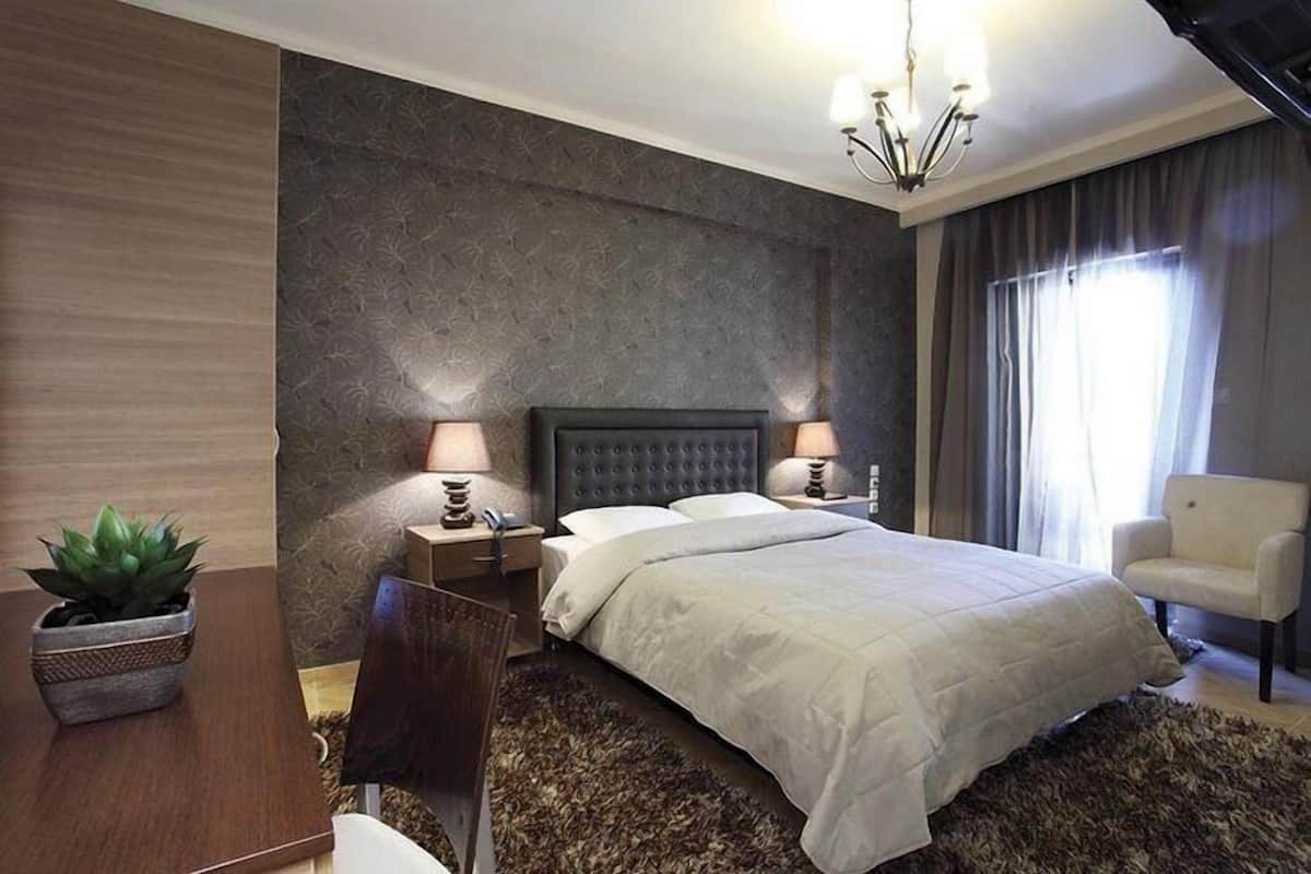 A modern bedroom with a large bed, two bedside tables with lamps, a chair, and a potted plant.