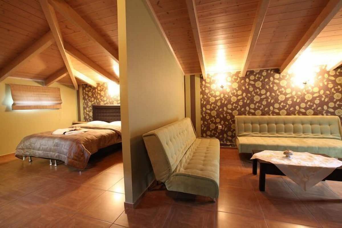A cozy attic bedroom with a vaulted ceiling, a bed, a sofa, and a small table.