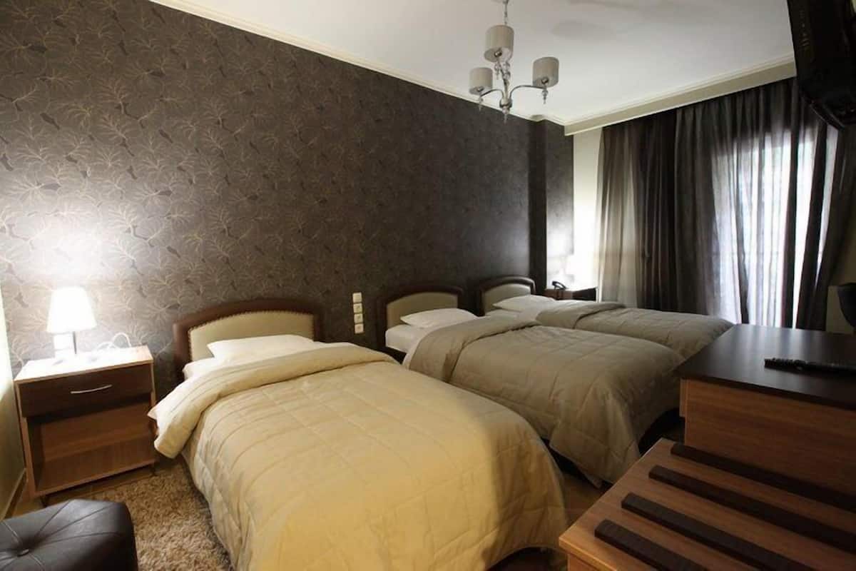 A hotel room with two beds, a desk, a lamp, and a chandelier.