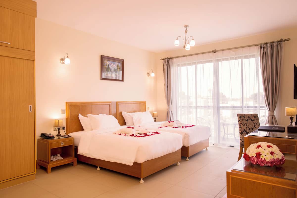 A hotel room with two beds, a desk, a chair, and a large window with curtains.
