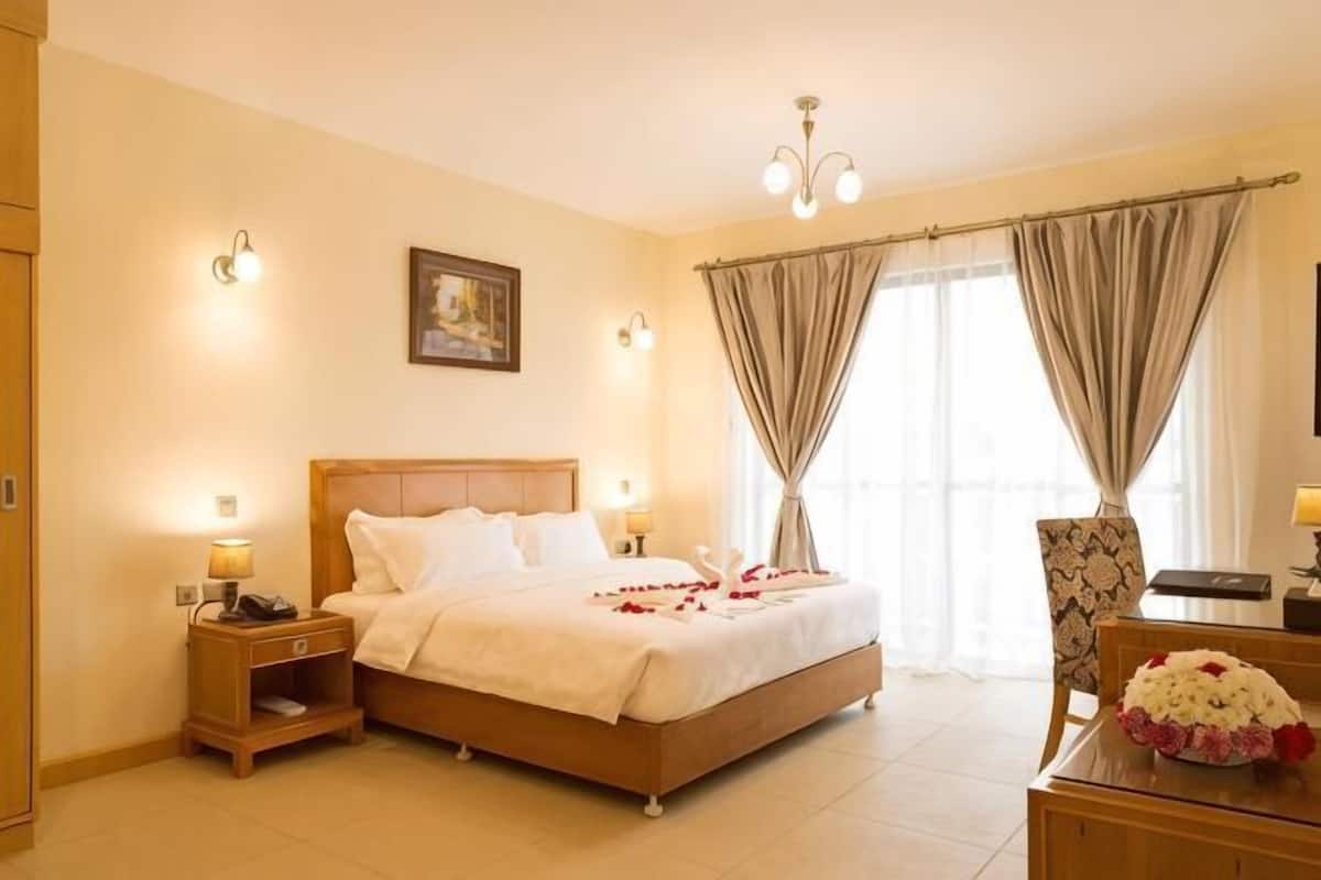 A hotel room with a bed, bedside tables, a desk, a chair, and a window with curtains.