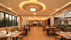 A spacious restaurant with wooden tables and chairs, a central bar, and large windows offering views of the outdoors. - Lotos Inn & Suites, Nairobi (Nairobi)