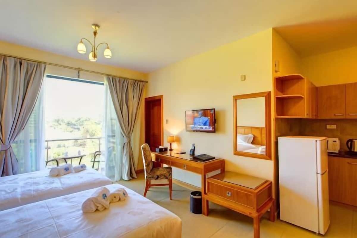 A hotel room with two beds, a desk, a TV, a refrigerator, and a balcony.