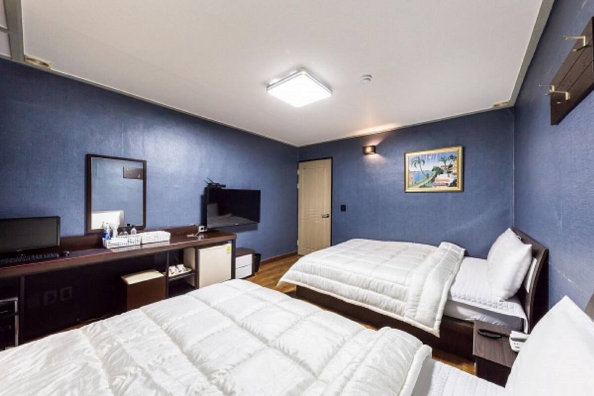Habitación de hotel con dos camas, un escritorio con computadora, un televisor y un cuadro en la pared.