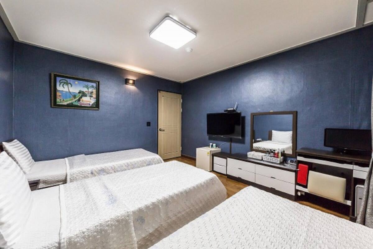 Habitación de hotel con dos camas, un televisor, un escritorio con computadora y un cuadro en la pared.
