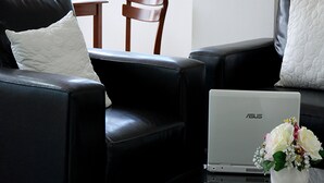 A modern living room with a black leather sofa, a white cushion, and a laptop on a glass table.