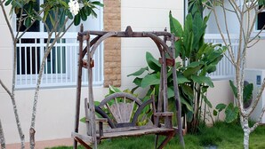 A rustic wooden swing set in a garden with a white fence and large green plants.