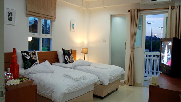 A hotel room with two beds, a TV, a window with curtains, and a balcony.