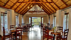 A spacious dining area with wooden tables and chairs, a high wooden ceiling, and large windows allowing natural light. - Thanda Manzi Country Hotel (Centurion)