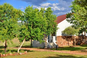 Una casa con pared de piedra y techo rojo, rodeada de árboles verdes y una zona con césped.