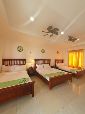 A hotel room with three wooden beds, a ceiling fan, and a bright yellow curtain. - Moalboal Tropics (Moalboal)