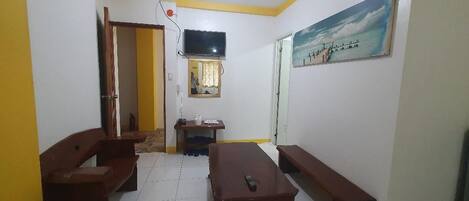 Una habitación con piso de baldosas, una mesa de madera, dos bancos, un televisor y un cuadro en la pared.