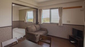 Una habitación con sofá, televisión, cama y ventana con cortinas.