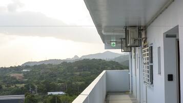 A balcony with a view of a mountainous landscape, a white building with a door and window, and a green directional sign.