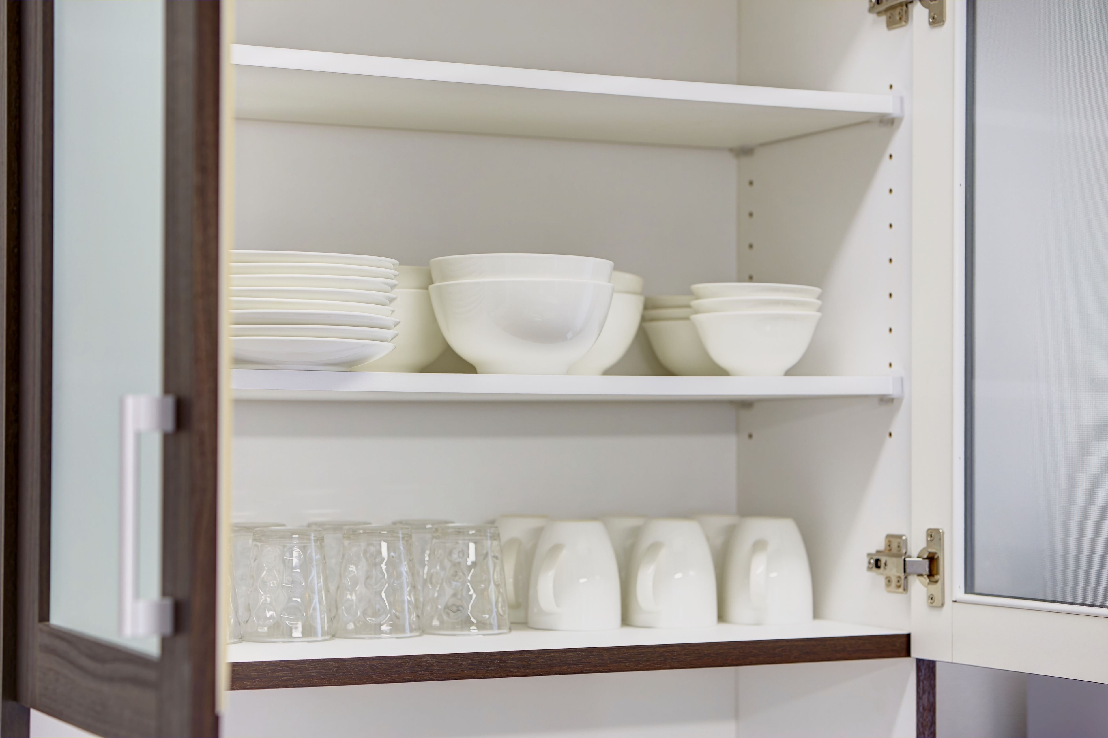 A white cabinet with shelves holding white bowls and clear glass cups.