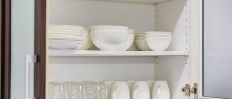A white cabinet with shelves holding white bowls and clear glass cups.