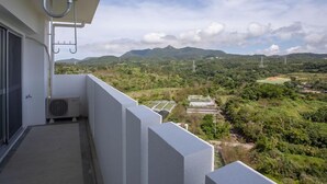 Un balcón con vistas a un paisaje montañoso, que incluye un campo deportivo y líneas eléctricas.