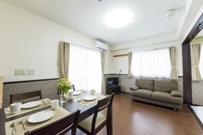A dining area with a table set for four, a sofa, and a television in a living room. - Condominium Resort Nago Grand Sedona (Nago)