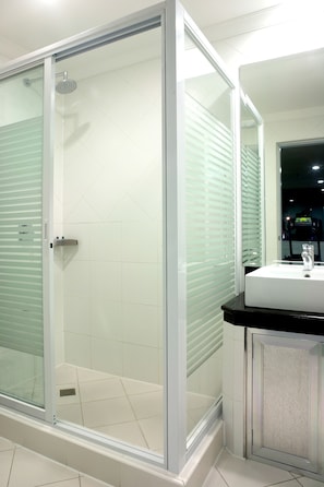 A modern bathroom with a glass-enclosed shower, a white sink, and a mirror. - Queens Hotel (Angeles City)