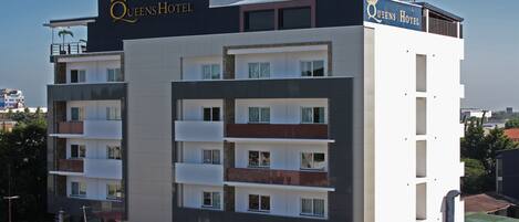 A multi-story hotel with balconies, a prominent crown logo, and the name 'Queens Hotel' on the facade.