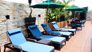 Eine Dachterrasse mit Korlounge-Möbeln, blauen Kissen, Steinmauern und grünen Sonnenschirmen.
