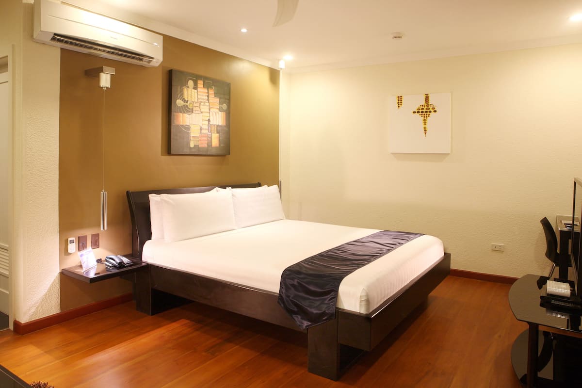 A hotel room with a bed, bedside table, lamp, and artwork on the walls.