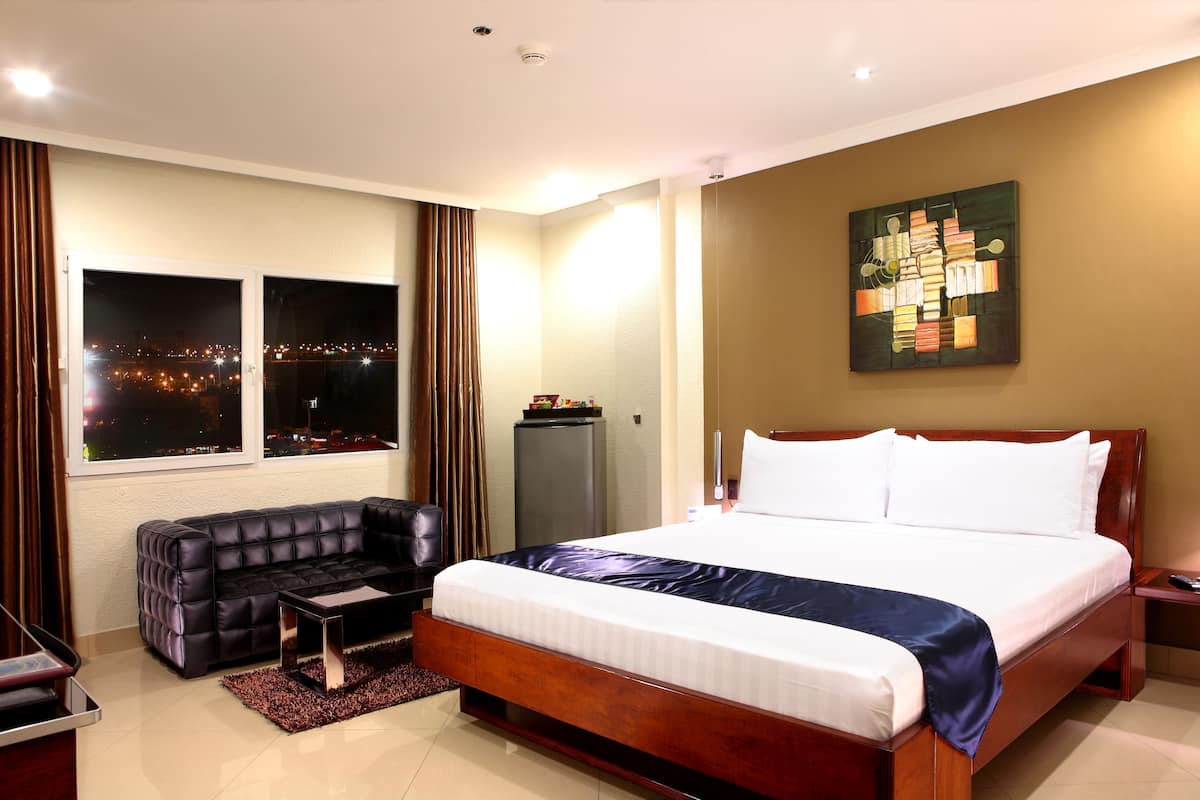 A hotel room with a large bed, a leather sofa, a desk, and a window with a city view.