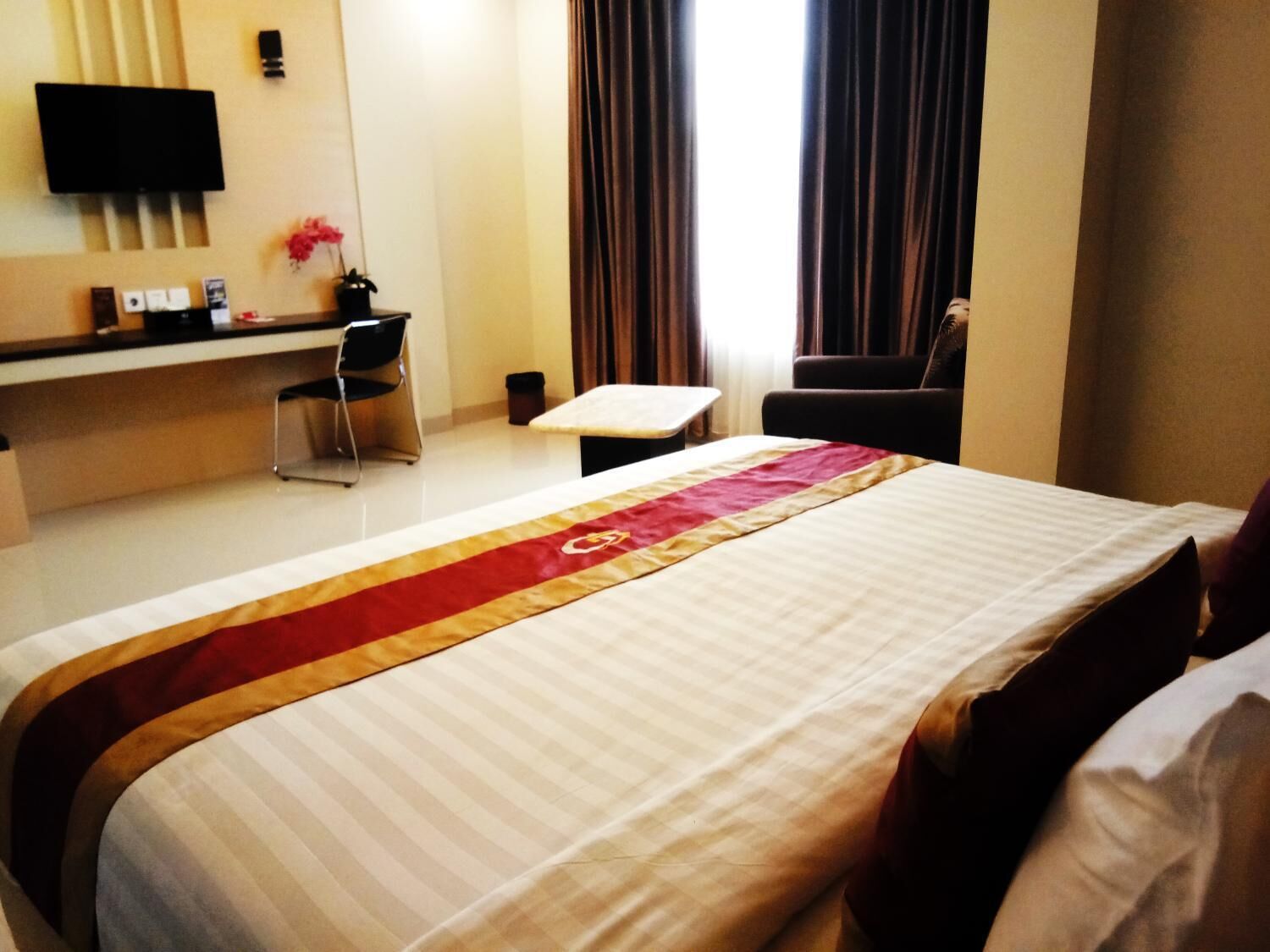 Ein Hotelzimmer mit Bett, Schreibtisch, Stuhl, Fernseher und einem Fenster mit Vorhängen.
