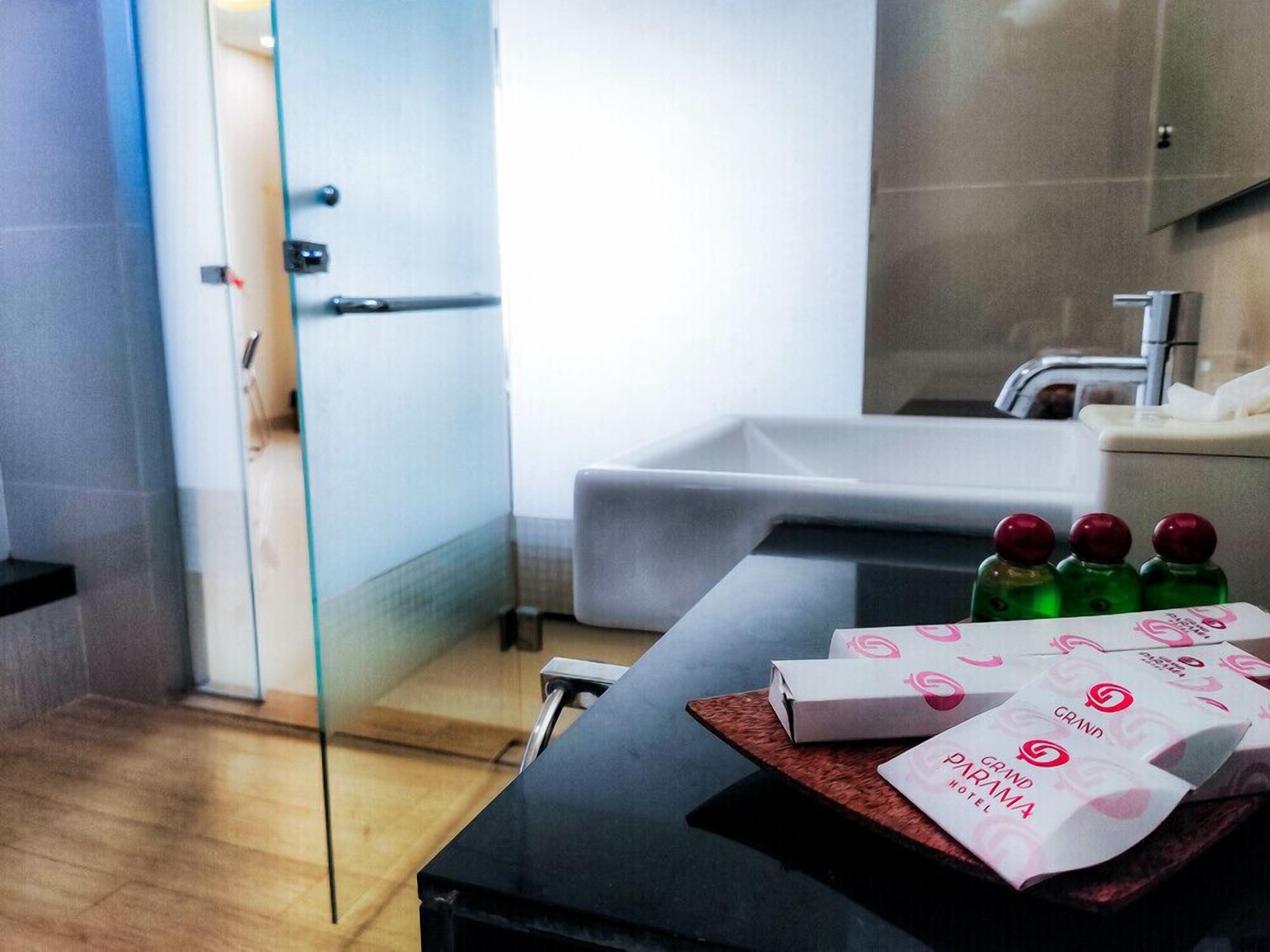 Baño de hotel con bañera, cabina de ducha de vidrio y lavabo. Hay artículos de aseo en la encimera.