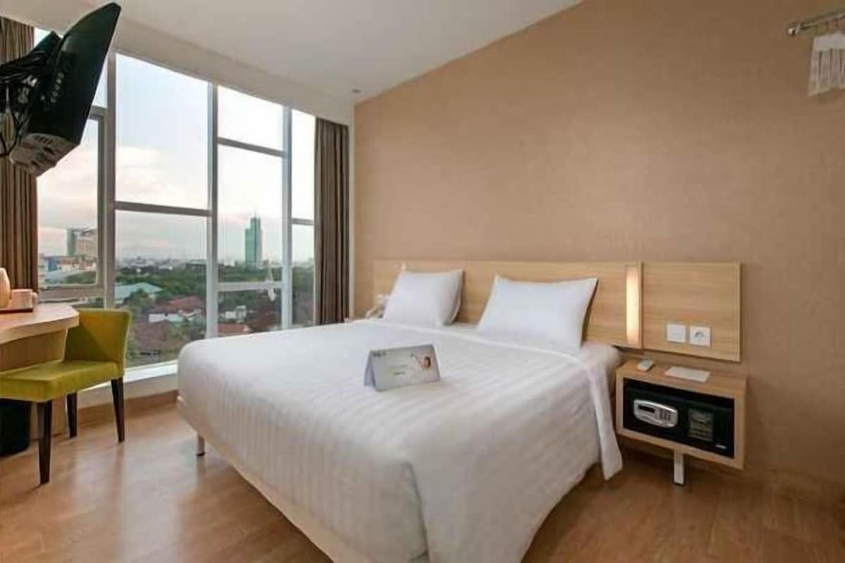 A hotel room with a large bed, a desk, a chair, and a view of the city.