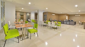 Un espace repas moderne avec plusieurs tables et chaises, un coin cuisine équipé d’appareils électroménagers et un sol carrelé, propre et bien entretenu.