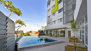 Une cour d’hôtel moderne dotée d’une piscine, d’un espace de détente extérieur et d’un bâtiment orné d’une enseigne verte bien visible.