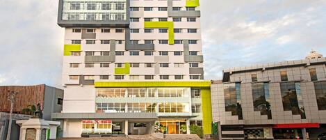 Un hôtel à plusieurs étages, doté d’un design moderne, avec une entrée imposante, une façade en verre et des éléments décoratifs verts.