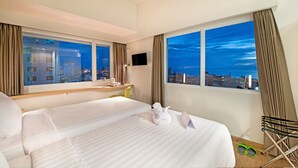 Une chambre d ’hôtel avec un grand lit, un bureau, une chaise et une vue sur le paysage urbain la nuit.